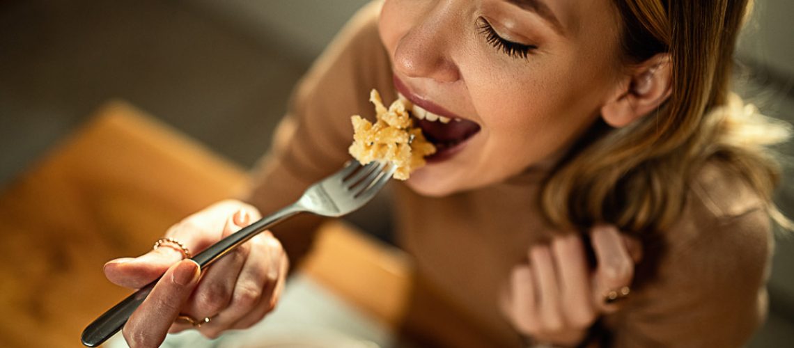 Close-up of happy woman eating pasta for dinner.