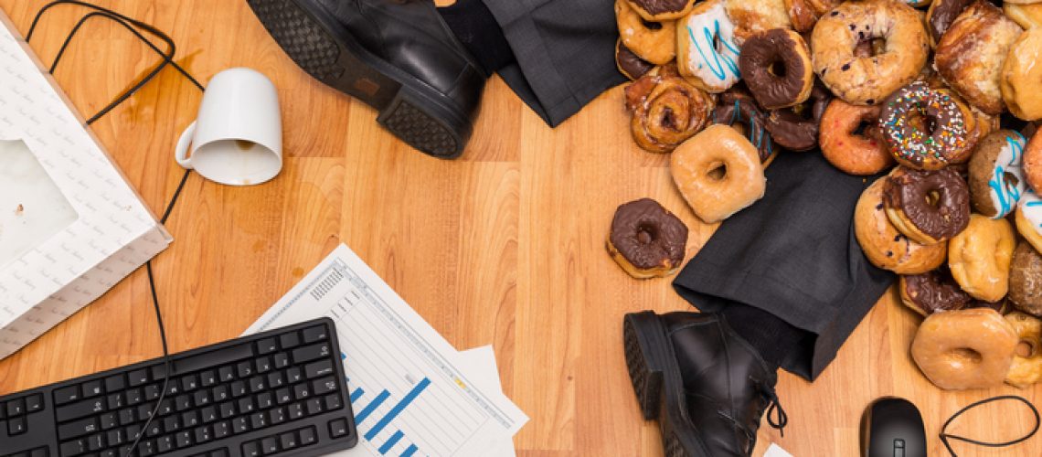Overeating at work concept - A business person is buried under a large pile of donuts at their desk.  They have spilled coffee, reports on the floor, and the computer on the floor.  Please see my portfolio for other business concept images.
